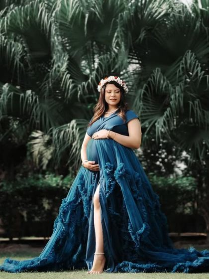 A beautiful outdoor portrait of an expecting mother in a blue gown, standing in front of lush palm trees. The natural setting provides a vibrant and tropical feel to the maternity photo.