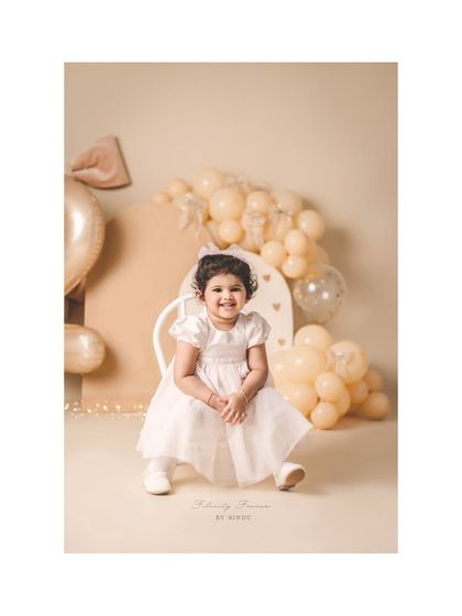 A lovely portrait of a two-year-old girl, surrounded by soft, neutral-colored balloons and decorations.