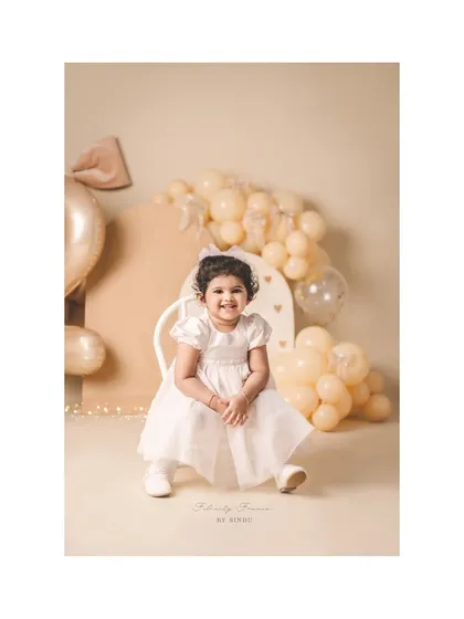 A lovely portrait of a two-year-old girl, surrounded by soft, neutral-colored balloons and decorations.