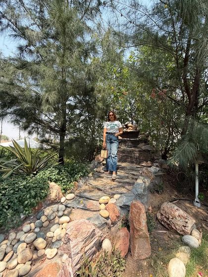 This full-length shot showcases the complete travel outfit. The bootcut jeans elongate the legs, while the simple tee and straw bag keep it casual and practical.