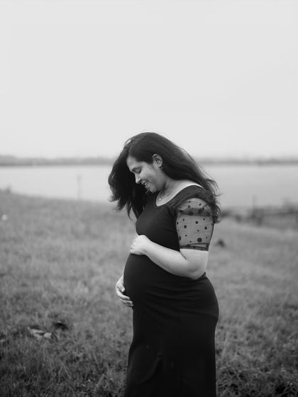 A quiet, contemplative black and white portrait. The mom-to-be looks down at her bump with a gentle smile, a private moment of connection with her baby.