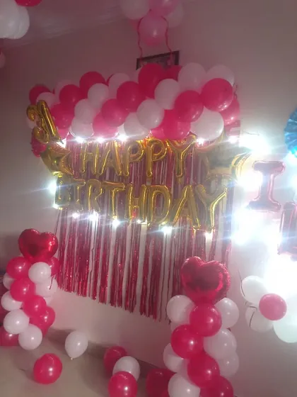 A pink and white birthday backdrop with a shimmer curtain, "Happy Birthday" foil balloons, and light-up balloon pillars.