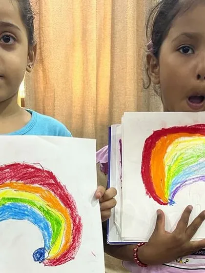 Two girls showing off their vibrant rainbow paintings. We encourage using bold colors and letting their imagination run free.