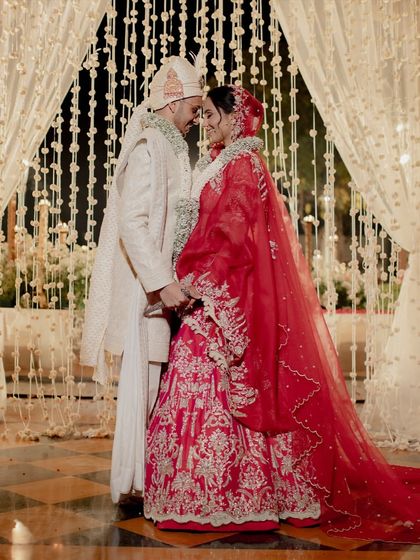 A quiet moment between the couple amidst the grandeur of their wedding day. The backdrop of cascading white florals and the soft glow of the lights create an atmosphere of pure romance.