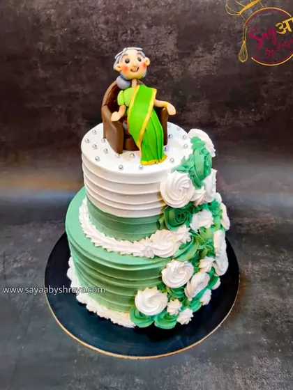 A two-tier cake in elegant green and white, topped with a sweet figurine of a grandmother sitting contentedly. This was designed to honor the matriarch of a family with grace and style.