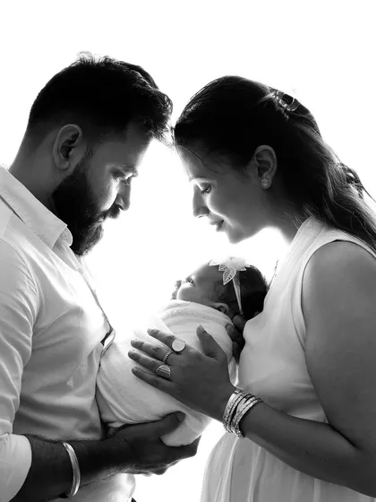 An intimate black and white portrait of new parents adoring their sleeping baby. The soft lighting and close framing create a timeless image of a family's first moments together.