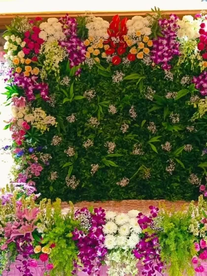 A lush floral wall created for Maghi Ganpati celebrations. This design uses a mix of colorful fresh flowers like orchids and lilies against a dense green backdrop to create a vibrant, garden-like feel.