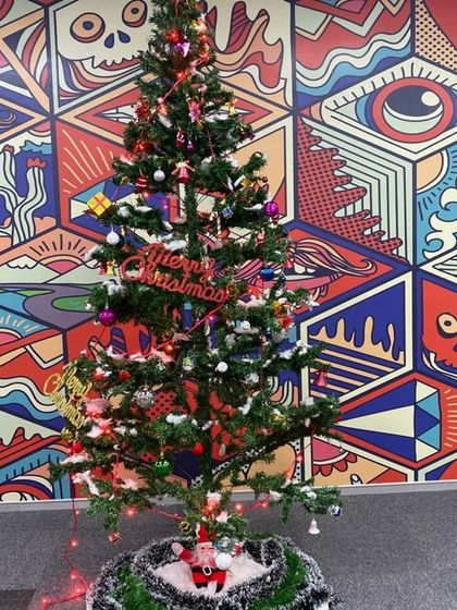 A close up of a fully decorated Christmas tree, complete with ornaments, lights, and a 'Merry Christmas' sign, ready for an office party.