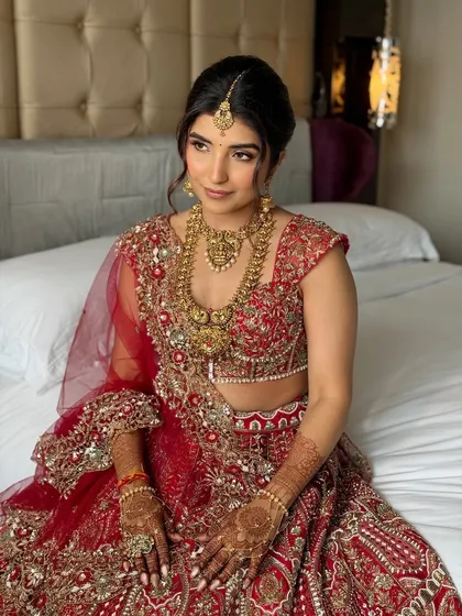 A full seated portrait showing the intricate work on the red lehenga and how the soft makeup balances the entire look.