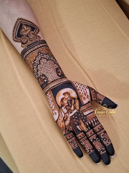 A single-hand close-up of a romantic Karwa Chauth portrait. The design captures a tender moment between a couple, framed by intricate patterns and a decorative diya motif on the forearm.