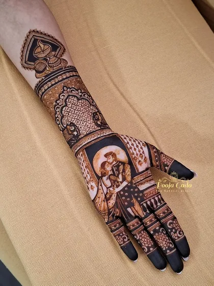 A single-hand close-up of a romantic Karwa Chauth portrait. The design captures a tender moment between a couple, framed by intricate patterns and a decorative diya motif on the forearm.