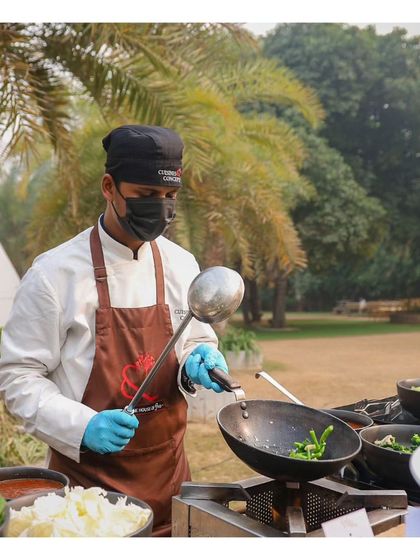 A chef at a live wok station, stir frying fresh vegetables for an Asian dish. The outdoor setting with palm trees adds to the relaxed, vibrant atmosphere of the event.