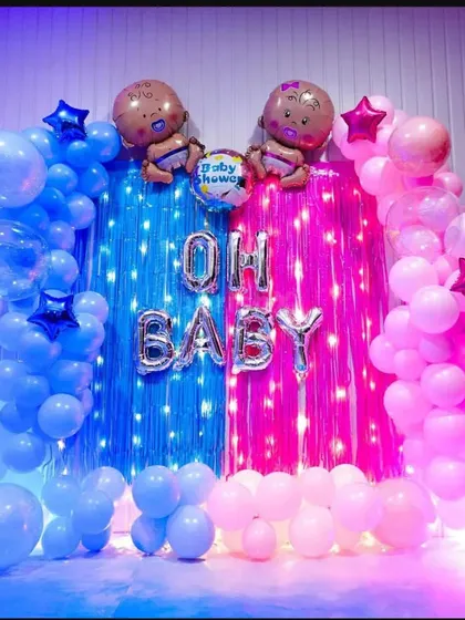 An "Oh Baby" gender reveal or baby shower backdrop with a dramatic flair. The blue and pink fringe curtains are framed by matching balloon garlands, creating a vibrant and colorful photo spot.