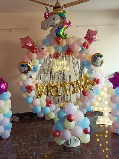 A unicorn-themed 4th birthday party with a full room setup. It includes a balloon arch with a unicorn head, a neon sign, a light-up number, and balloon pillars.