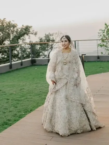 A full-length shot of the bride walking on a path, her elegant white lehenga flowing beautifully.