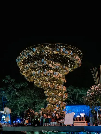A massive, tornado-shaped floral chandelier, lit with fairy lights, serves as a breathtaking centerpiece for the Sangeet, demonstrating our flair for creating unique, large-scale installations.