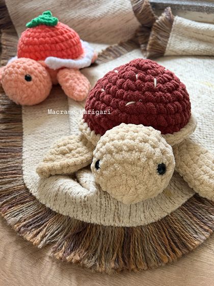 A close-up of our chunky yarn turtles. This pair features a strawberry-themed shell and a rich maroon shell, showcasing the creative designs we love to make.
