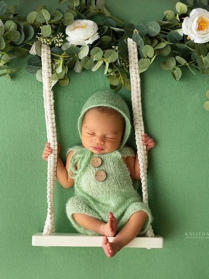 A six-day-old baby girl on a tiny swing, surrounded by greenery. This creative setup adds a touch of whimsy and magic to the newborn portrait.