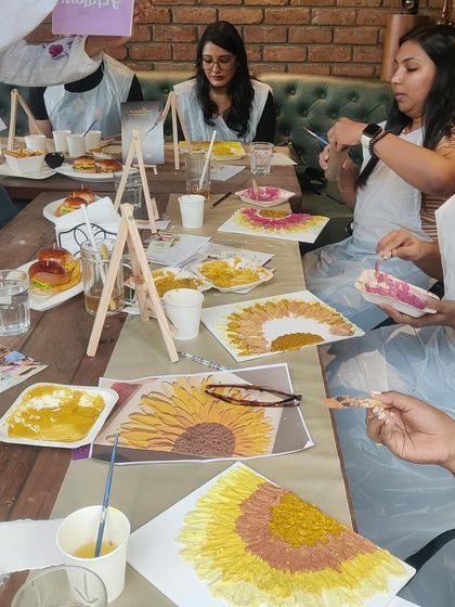 A table full of participants, each focused on their own sunflower texture painting. The room is always buzzing with quiet, creative energy.
