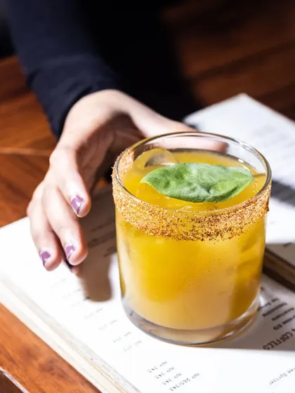 The Ahhh!!! Man-go mocktail is a taste of summer in a glass. This vibrant yellow drink, garnished with a fresh basil leaf, brings back memories of sunny days with every sip.