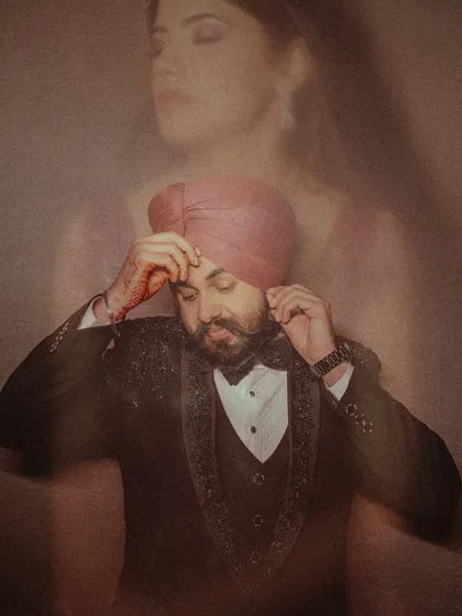A creative double-exposure shot of the groom, Sanjit, adjusting his turban, with the bride's image softly overlaid, symbolizing their union.