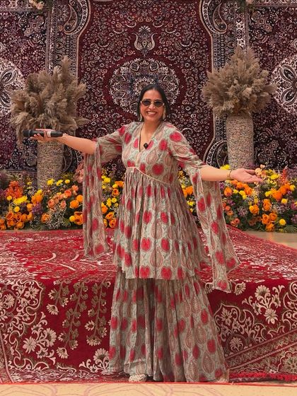On stage in a beautiful printed sharara set. The flowing sleeves and traditional pattern make it an excellent choice for hosting Indian wedding functions.