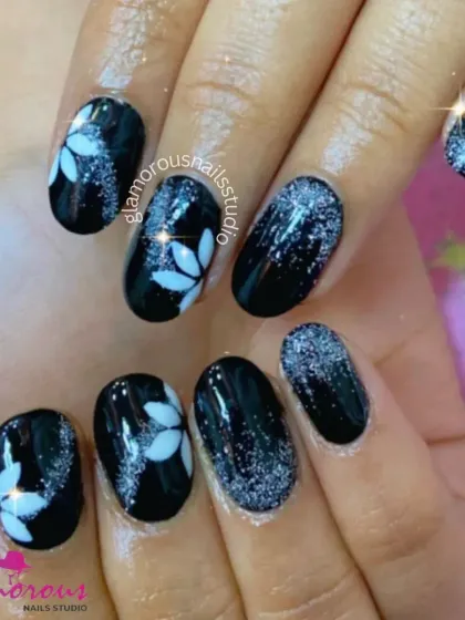 A striking contrast of glossy black nails with silver glitter and accent nails featuring a crisp, white floral design.