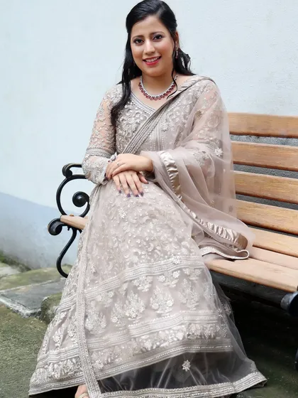 A full-length seated portrait showing the intricate details of her embroidered Anarkali gown. The makeup is elegant and refined.