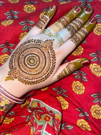 A classic mandala design with a leafy border, shown here with fresh henna paste. The details on the fingers complement the central pattern perfectly.