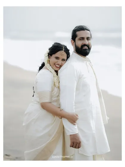A happy portrait of the couple on the beach, dressed in traditional white Kerala wedding attire.