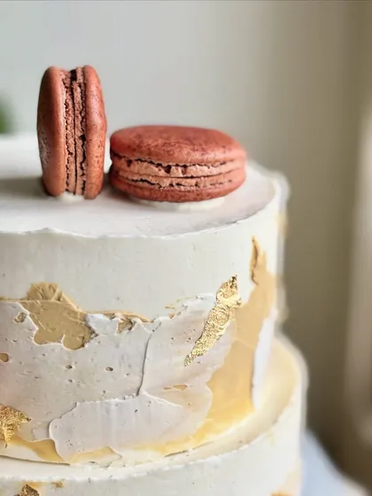 A detail shot focusing on the top of the gold leaf cake, showing the perfect texture of the macarons and the artistic application of the edible gold.