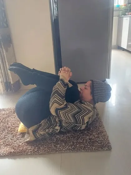 A senior client practices Pawanmuktasana (Wind-Relieving Pose) during a personal session at her home. This gentle pose is excellent for improving digestion and releasing tension in the lower back.