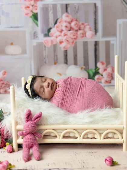 Sleeping soundly in a miniature bed, this newborn is surrounded by soft pink flowers. These styled setups create beautiful, dreamy portraits.