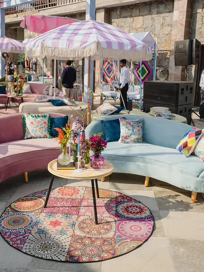 Pastel perfection for a Haldi. This lounge area features curved sofas in soft pink and blue, with colorful printed rugs and floral centerpieces, creating an elegant and whimsical seating arrangement.