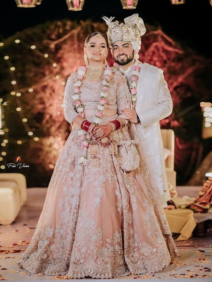 A classic full-length portrait of the newlyweds against a backdrop of festive lights, looking regal in their coordinated outfits.