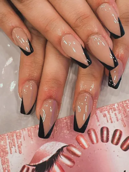 A modern twist on a classic style. These long, coffin-shaped nails feature a clean nude base with sharp, black V-shaped French tips, creating a chic and edgy geometric nail art design.