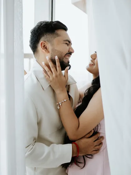 A moment of pure, uninhibited laughter between a couple. This candid shot, framed by soft curtains, captures the playful and joyful side of their relationship perfectly.