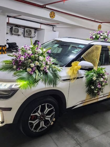 This Kia Seltos is decorated with beautiful bouquets of white roses, purple orchids, and palm leaves. The addition of gold fabric draping on the sides adds a touch of glamour to the wedding car.