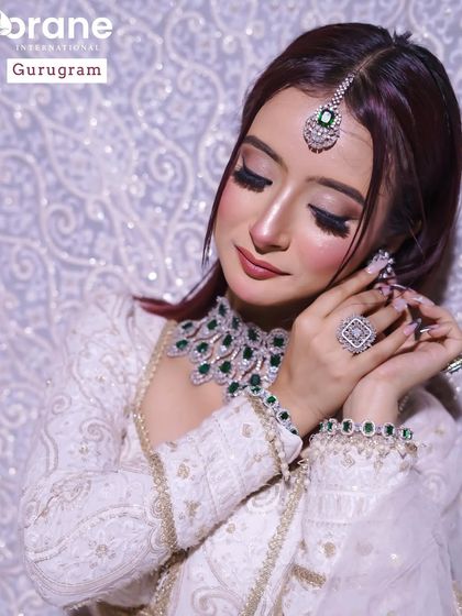 A student portfolio piece featuring a soft glam look with a white and gold outfit. The emerald jewelry adds a beautiful pop of color that the makeup subtly complements.