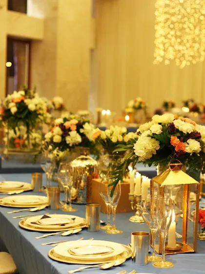 A sophisticated table setting with a blue tablecloth, gold lanterns, and elegant floral centerpieces. We fulfill every desire, from specific catering needs to stylized table decor.
