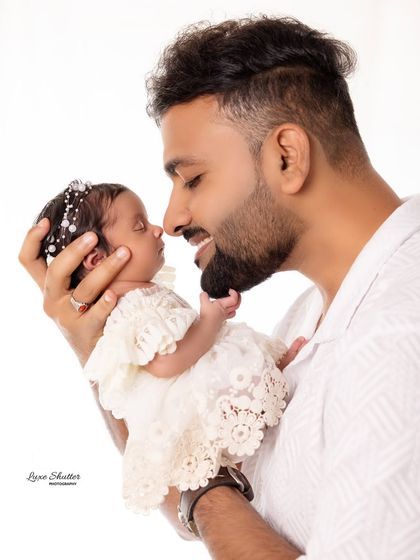 A beautiful close-up of a father and his newborn daughter. The baby's delicate lace outfit and headband add a touch of sweetness to the shot.