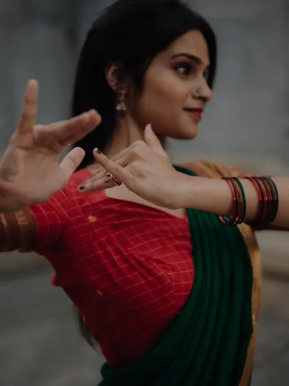 A close-up shot focusing on the dancer's expressive hands and traditional attire. The dark background and focused lighting create a moody and artistic portrait.