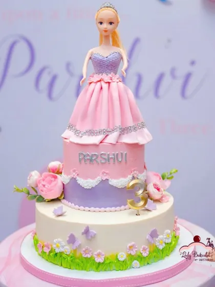 A classic doll cake, perfect for a princess party. This two-tier design features a beautiful doll with a flowing gown made of pink and purple buttercream and delicate sugar flowers.