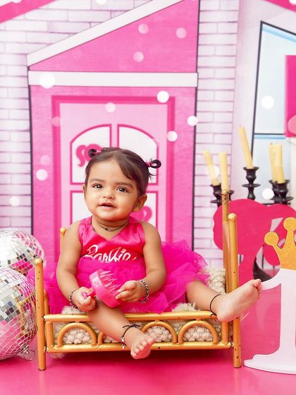 A Barbie girl in her Barbie world. Sitting on a miniature bed in her pink dream house, this little one is living a fantasy for her first birthday shoot.