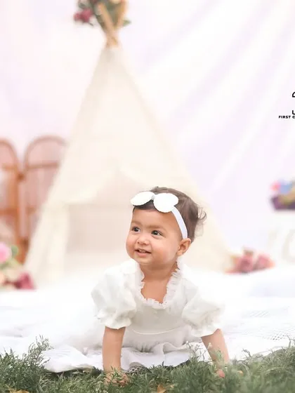 A beautiful shot of a baby girl crawling through the grass in a whimsical, white teepee setup. The natural foreground adds depth and texture to the photo.