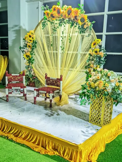 A lovely Haldi stage decorated with sunflowers and yellow drapes, featuring traditional low wooden chairs (bajot) for the ceremony.