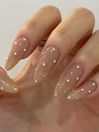 A simple but glamorous set with long, sheer nude stiletto nails and scattered rhinestones.