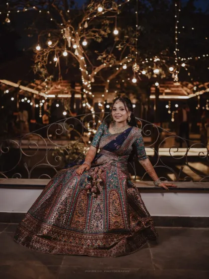 A full-length portrait of the bride seated, showcasing the stunning detail and grandeur of her bridal lehenga.