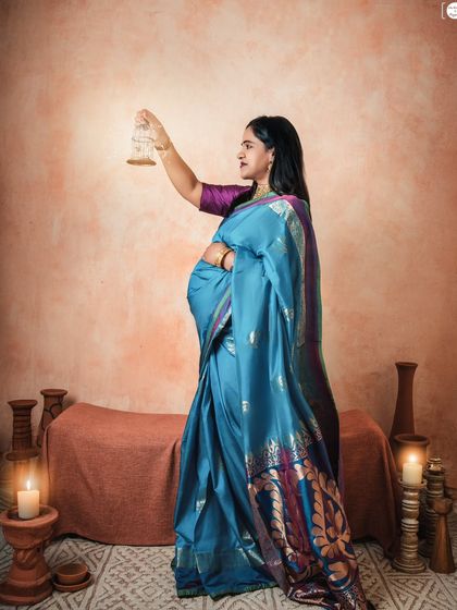 A graceful profile shot in a stunning blue saree. The warm, candle-lit setting with terracotta props complements the richness of traditional Indian textiles.