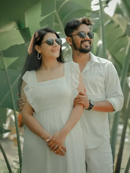 A fun and carefree moment captured against a backdrop of lush tropical leaves. The couple, dressed in matching white, shares a laugh, showcasing the relaxed and joyful side of their relationship.